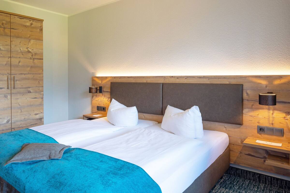 Een hotelkamer met een groot bed, een houten garderobe, bedlampjes en een hoofdeinde met ingebouwde verlichting.