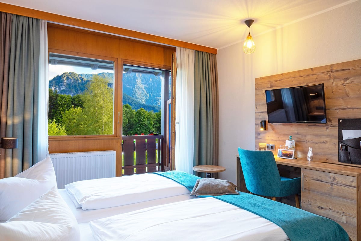 Een hotelkamer met een bed, een bureau, een stoel, een televisie en uitzicht op bergen.