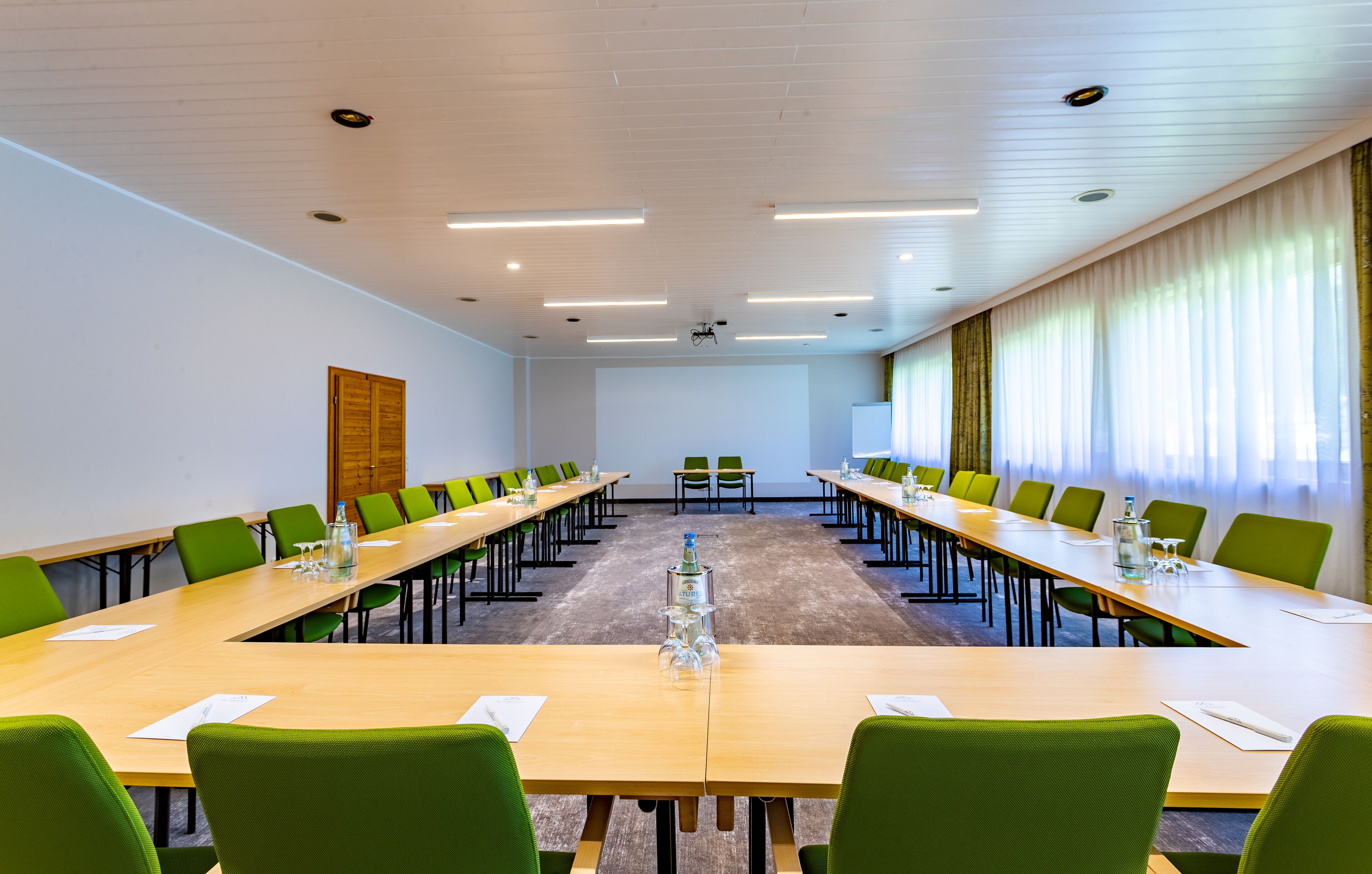 A conference room with long tables, green chairs, and a wooden door.