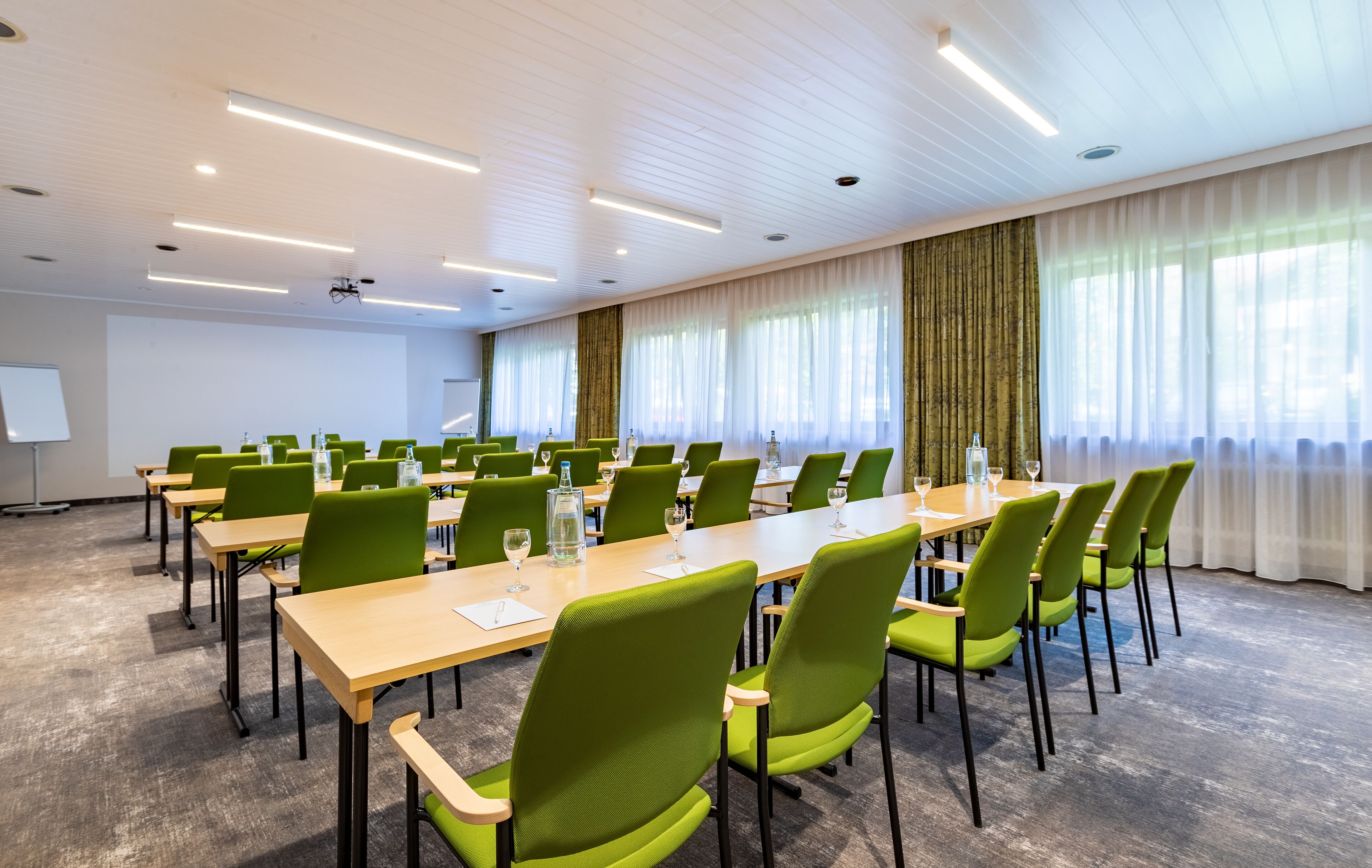 A conference room with long tables, green chairs, and a whiteboard.