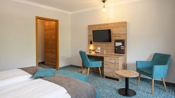 A hotel room with a bed, two chairs, a desk with a computer, a TV, and a coffee machine.