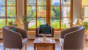 A room with two armchairs, a wooden coffee table, and large windows offering a view of a garden and a building. - Das Wiesgauer - Alpenhotel Inzell (Inzell)