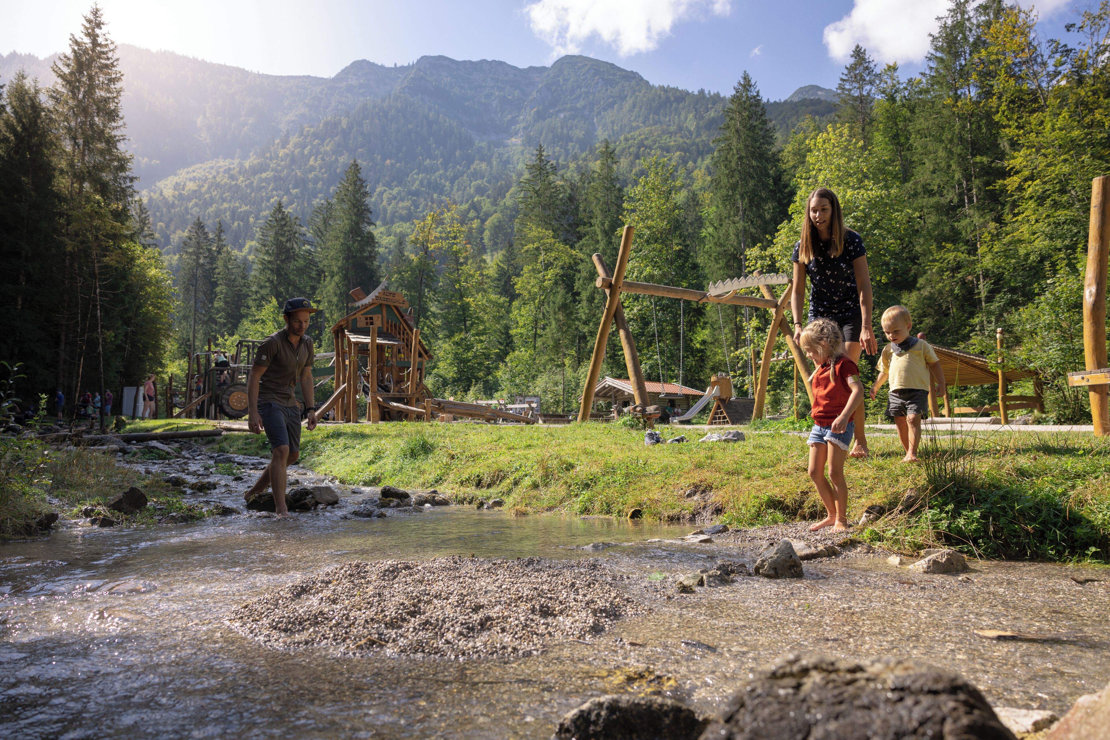 A wooden play structure in a forested area with a stream.