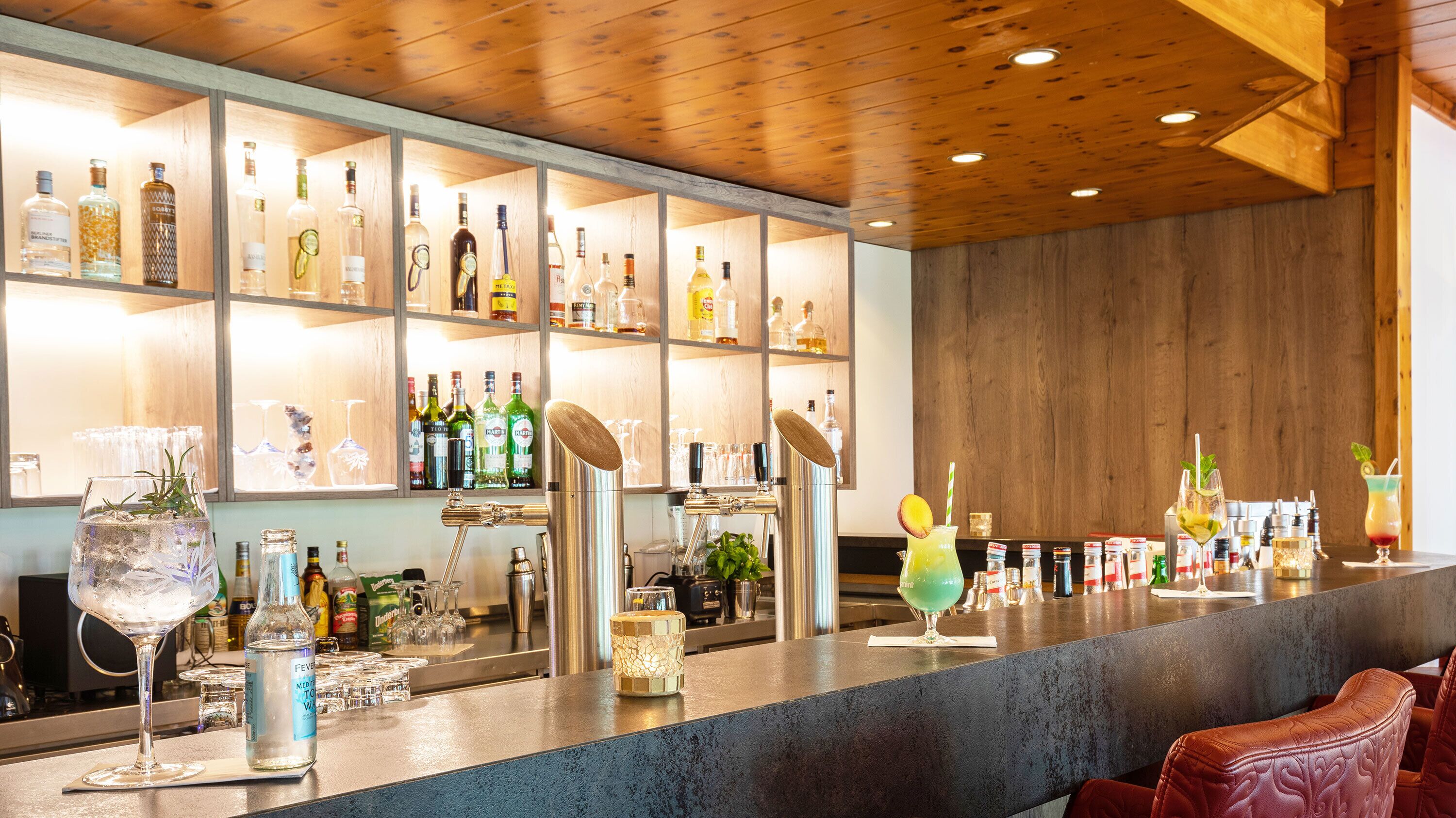 A bar area with shelves of liquor bottles, a bar counter, and bar stools.