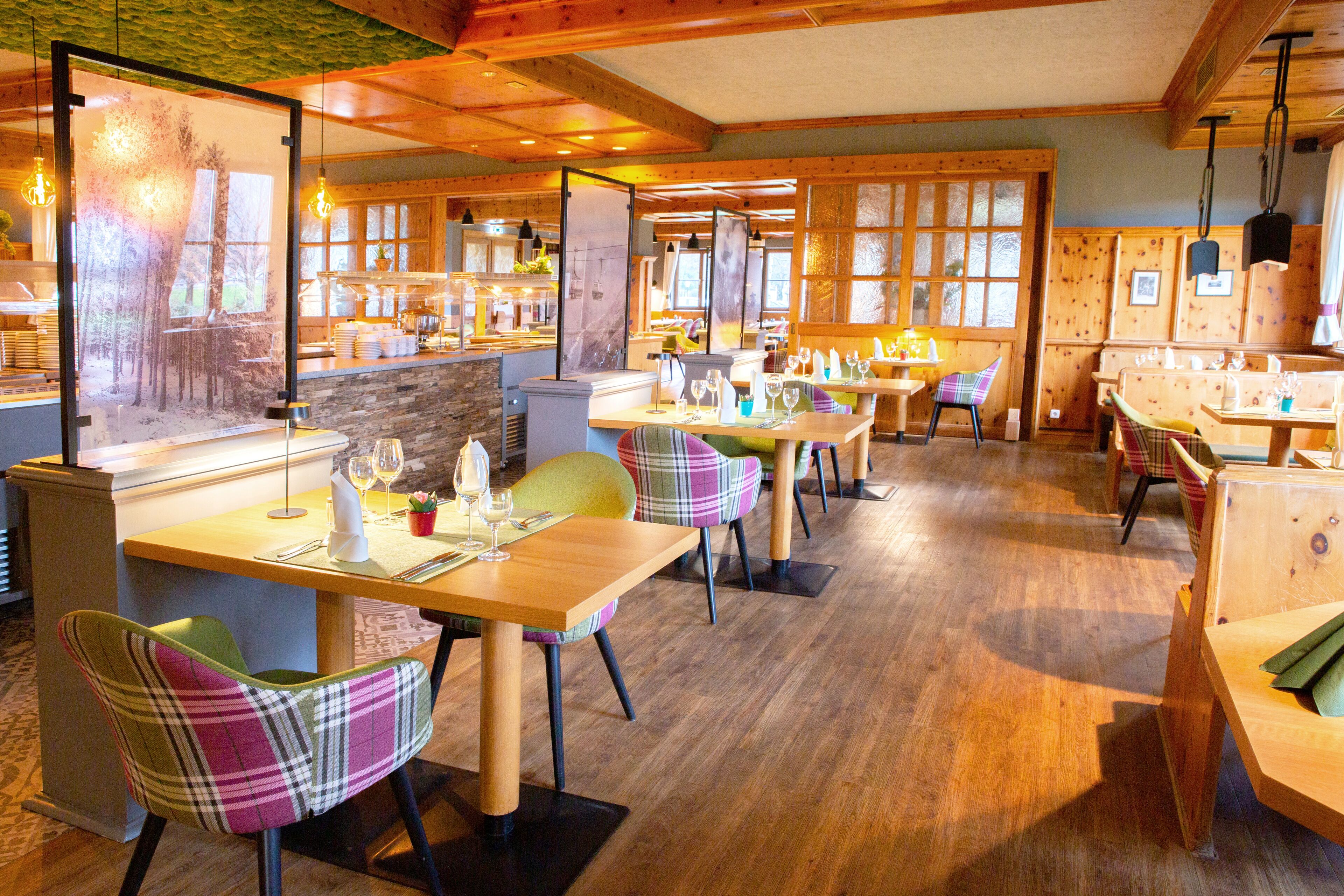 A restaurant with wooden tables and chairs, a stone counter, and large windows.
