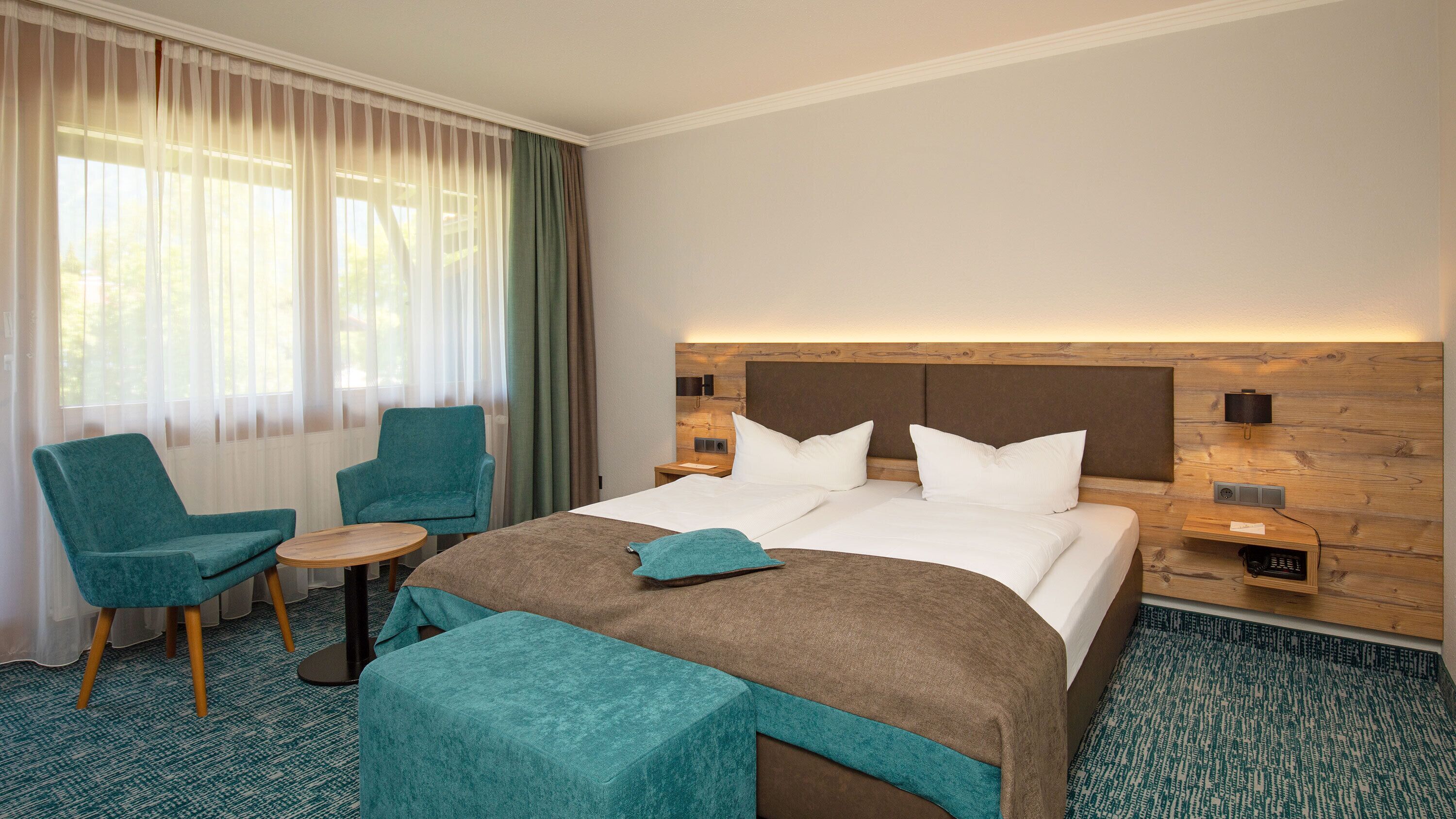 Ein Hotelzimmer mit einem großen Bett, zwei Sesseln, einem kleinen Tisch und einem Holzkopfende.