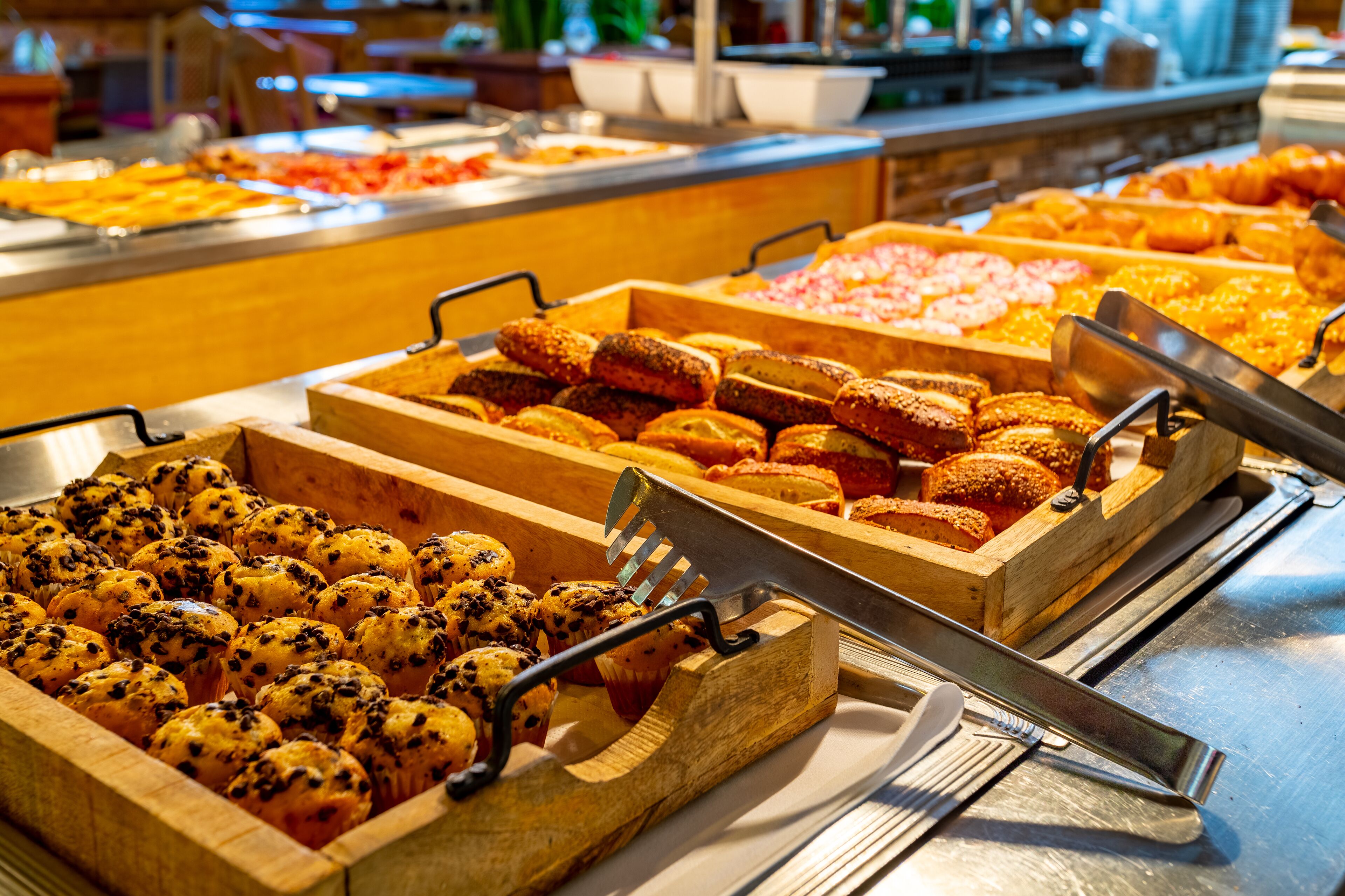 A buffet with various food items in wooden trays, including muffins and pastries.
