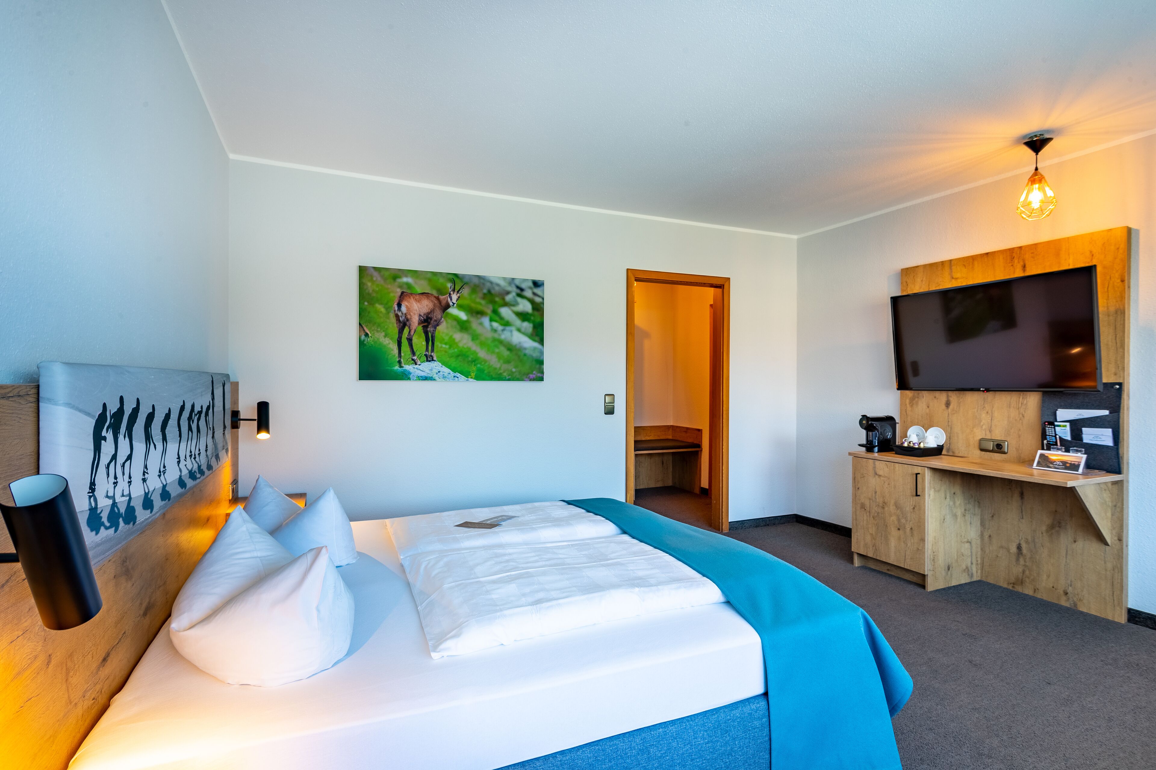 Ein modernes Hotelzimmer mit einem großen Bett, einem Wand-Fernseher und einer Holzkabine mit einer Kaffeemaschine.