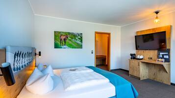 Ein modernes Hotelzimmer mit einem großen Bett, einem Wand-Fernseher und einer Holzkabine mit einer Kaffeemaschine.