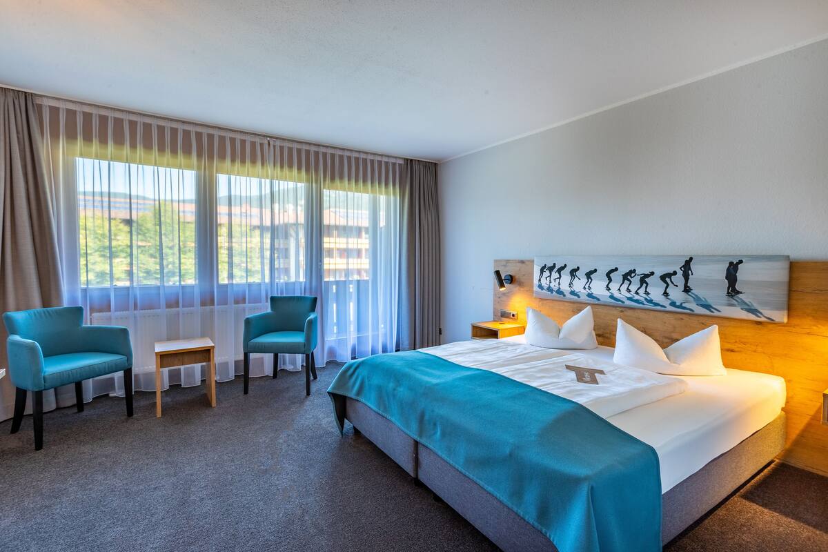 Een hotelkamer met een groot bed, twee stoelen, een kleine tafel en een schilderij aan de muur.