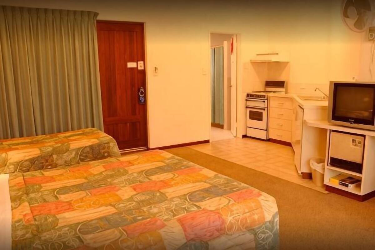 A hotel room with two beds, a kitchenette, a television, and a door.