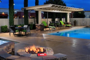 An outdoor pool area with a fire pit, lounge chairs, and a covered seating area. - Hampton Inn & Suites Las Vegas South (Henderson)