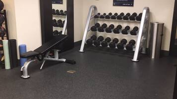 Un gimnasio con una banca, mancuernas y un espejo.
