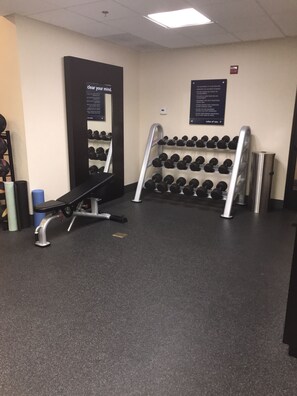A gym with a bench, dumbbells, and a mirror. - Hampton Inn & Suites Las Vegas South (Henderson)