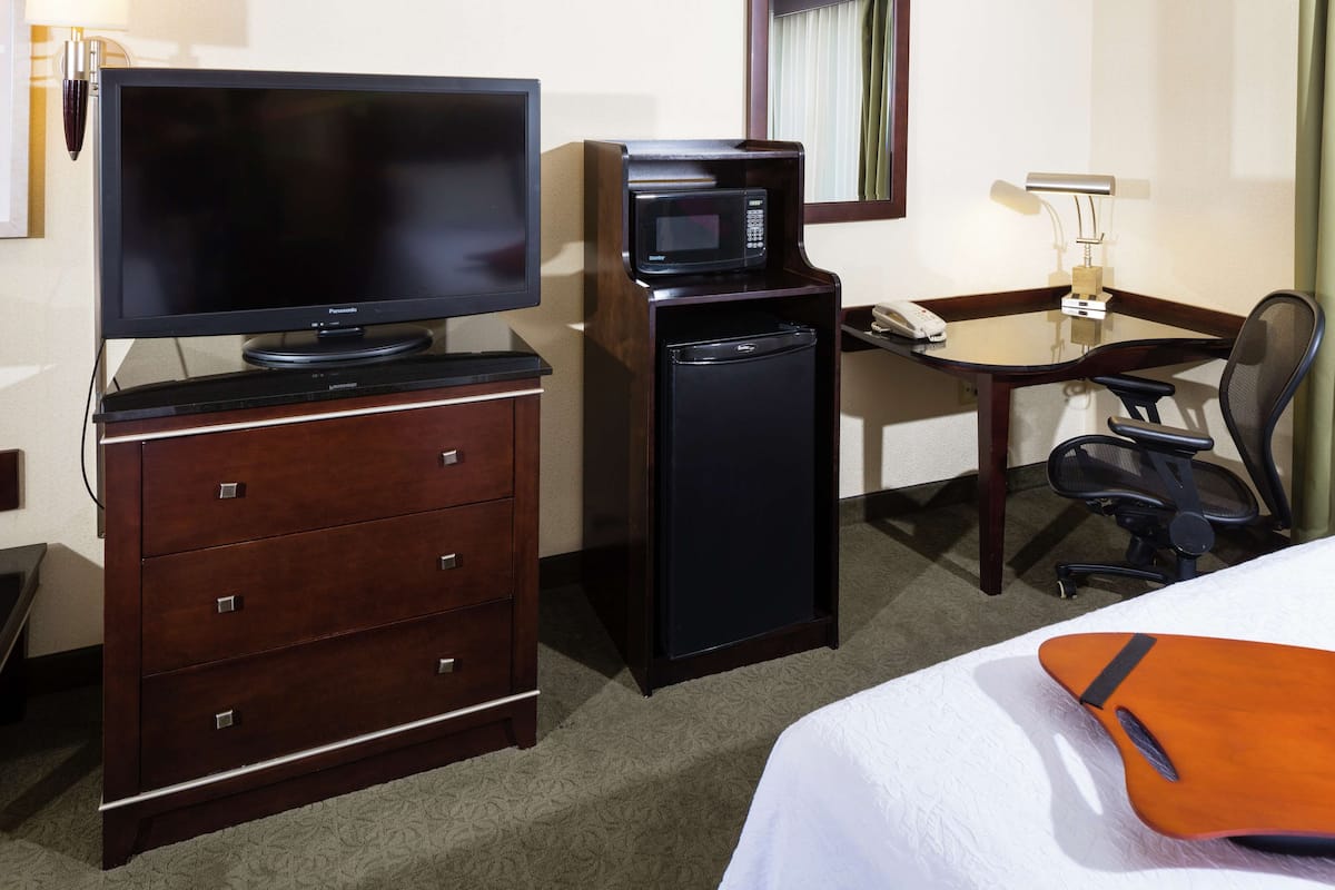 Quarto de hotel com televisão de tela plana, micro-ondas, escrivaninha com cadeira e cama com travesseiro laranja.