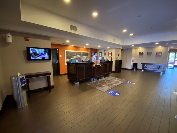 A hotel reception area with a reception desk, a television mounted on the wall, and a large poster. - Hampton Inn & Suites Las Vegas South (Henderson)