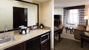 A hotel room with a kitchenette, a large mirror, a dining area with a table and chairs, a TV, and a window with curtains. - Hampton Inn & Suites Las Vegas South (Henderson)