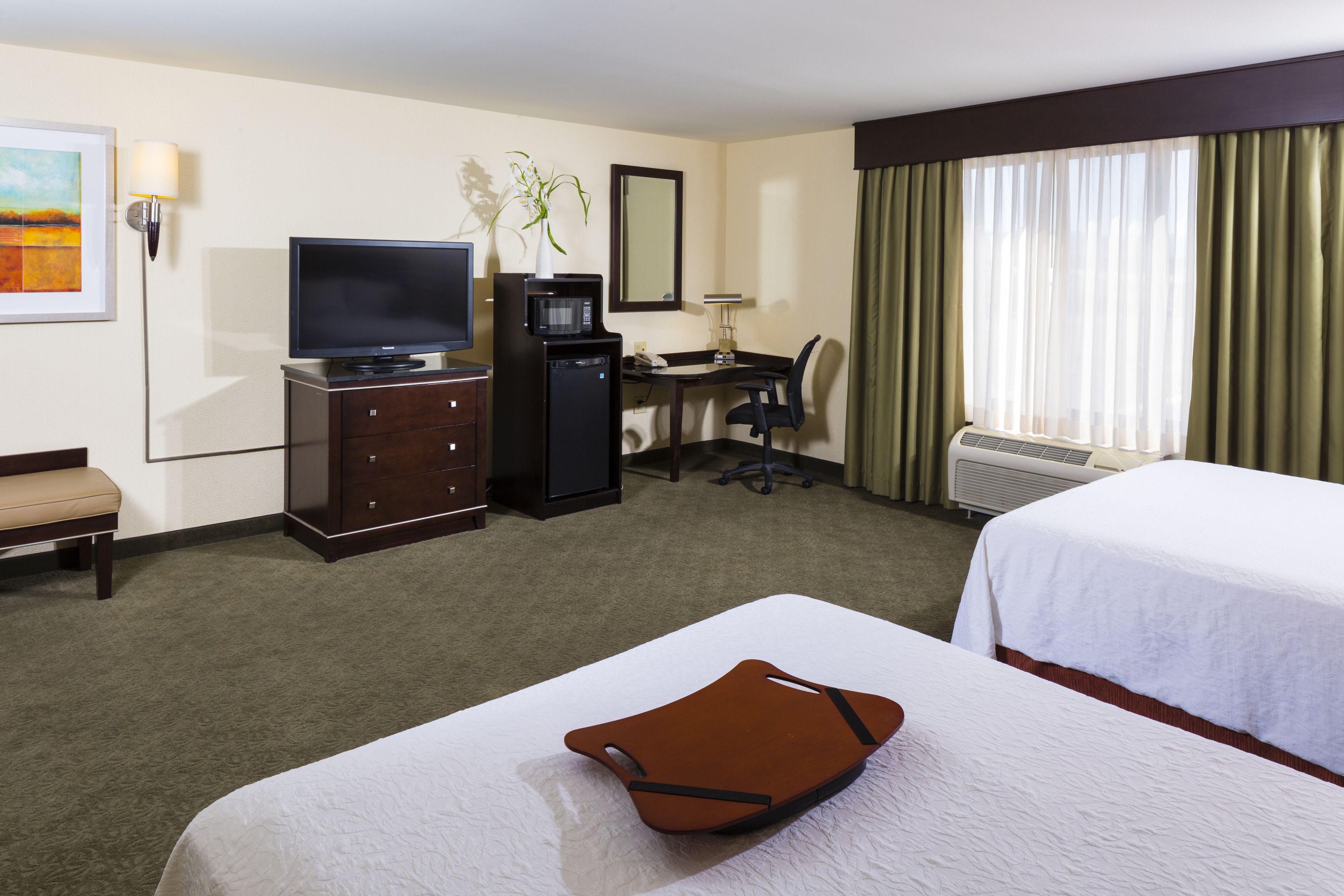 A hotel room with a bed, a desk with a computer, a television, and a small kitchenette.