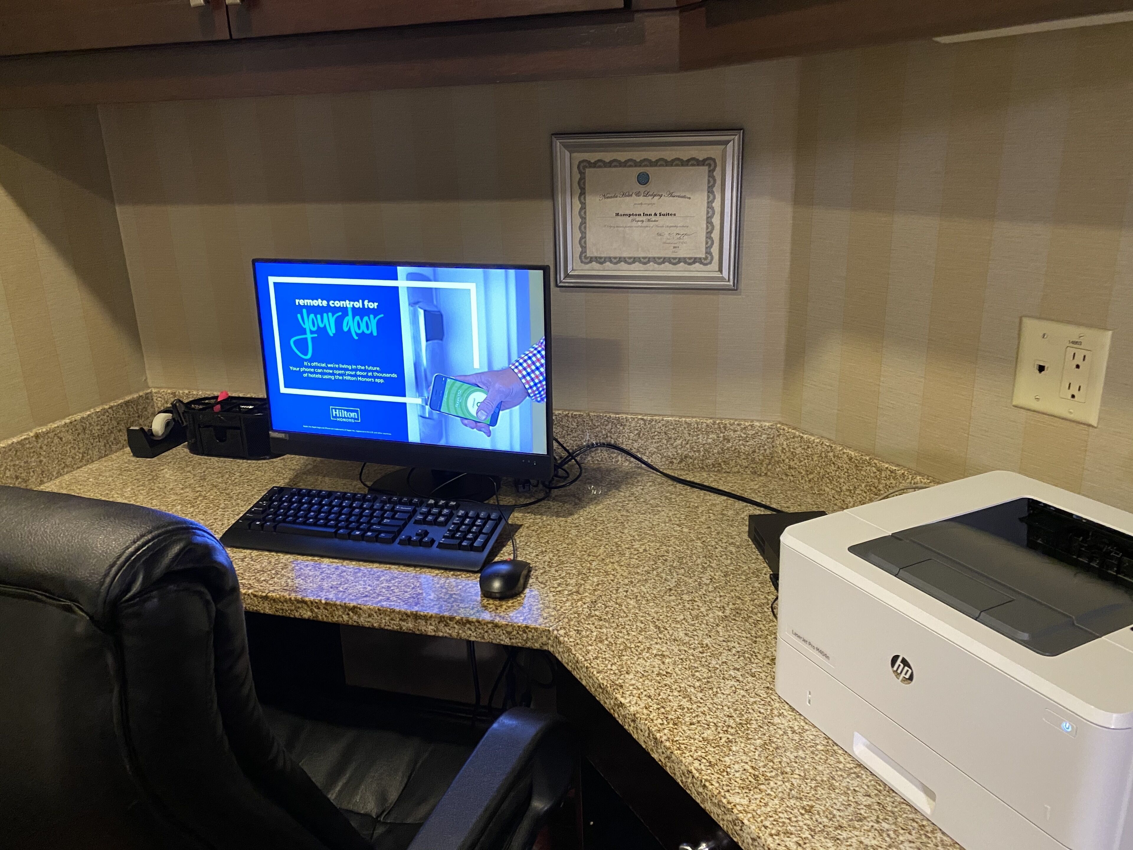 Ufficio di un hotel con un computer, tastiera, mouse e una stampante HP su un piano di granito.