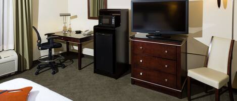 Una habitación de hotel con cama, escritorio con computadora, televisor, microondas, silla y lámpara.