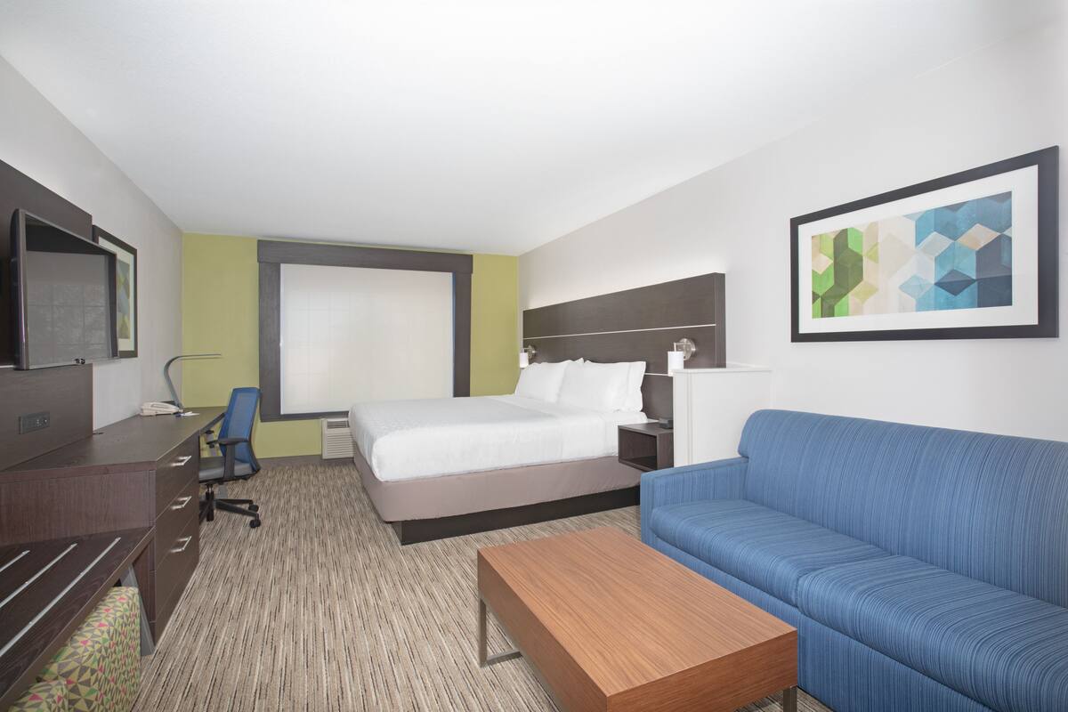 A hotel room with a bed, a desk, a chair, a sofa, and a TV.