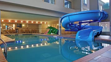 An indoor swimming pool with a water slide, seating area, and a lifeguard stand.