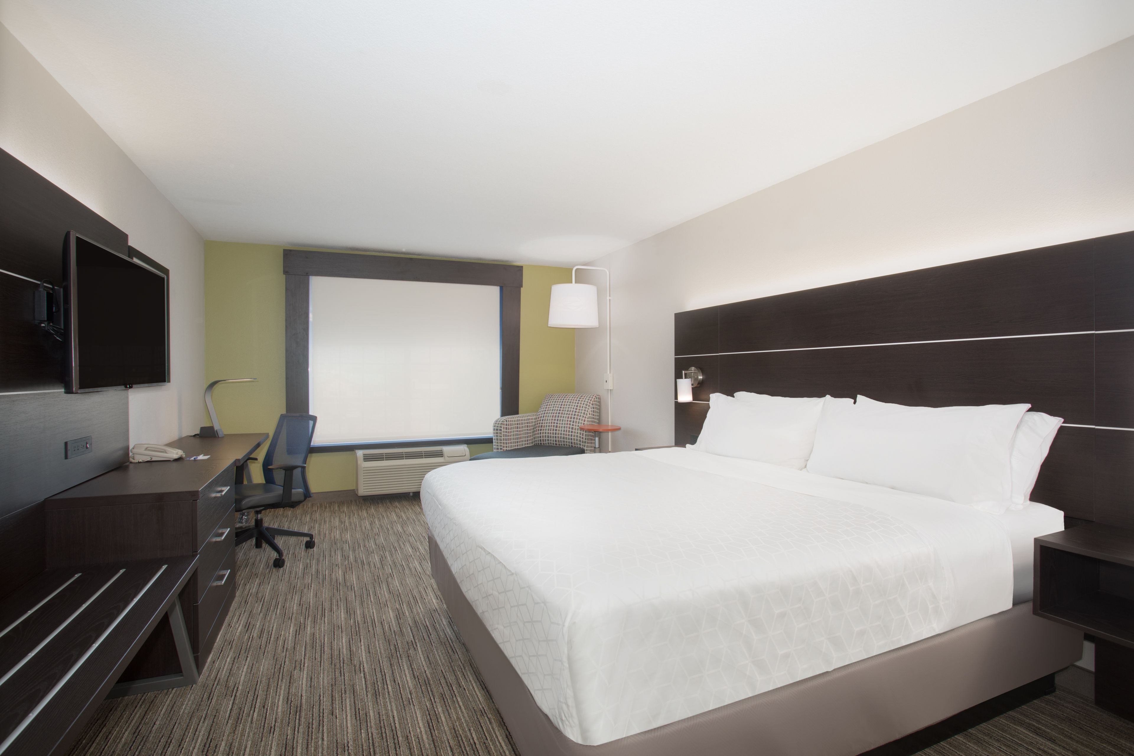 A hotel room with a large bed, a desk with a chair, a television, and a window with blinds.