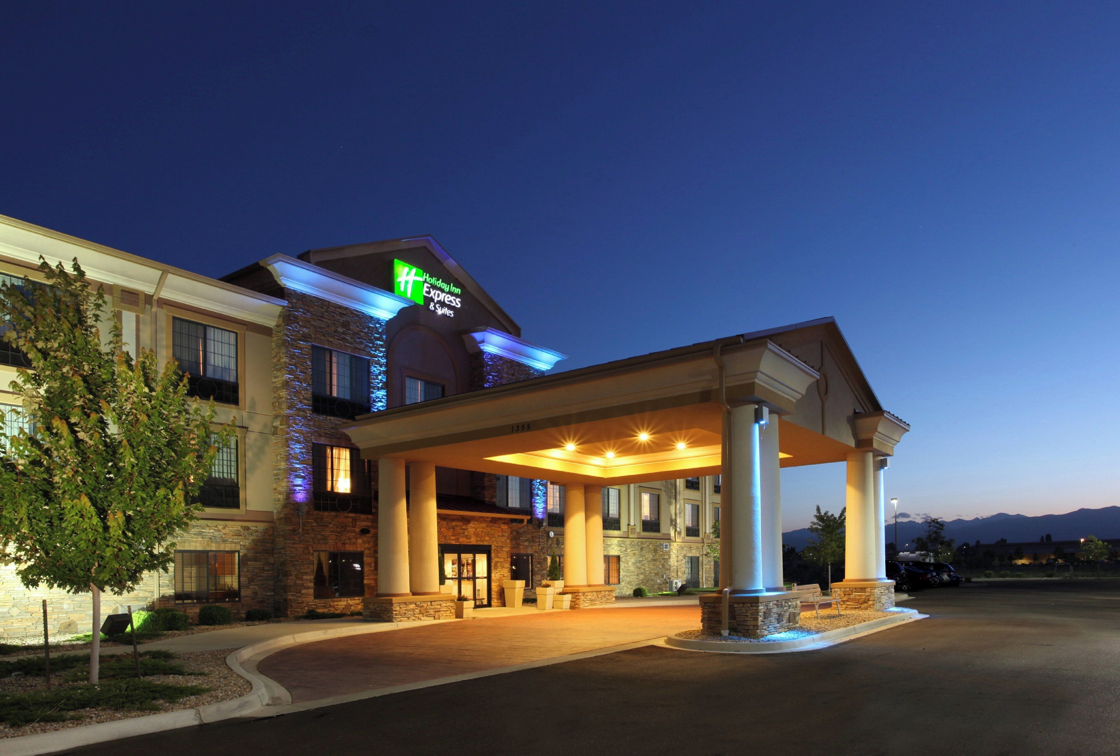 Un hôtel Holiday Inn Express & Suites doté d’une façade en pierre, d’une entrée couverte et offrant une vue sur un ciel dégagé au crépuscule.