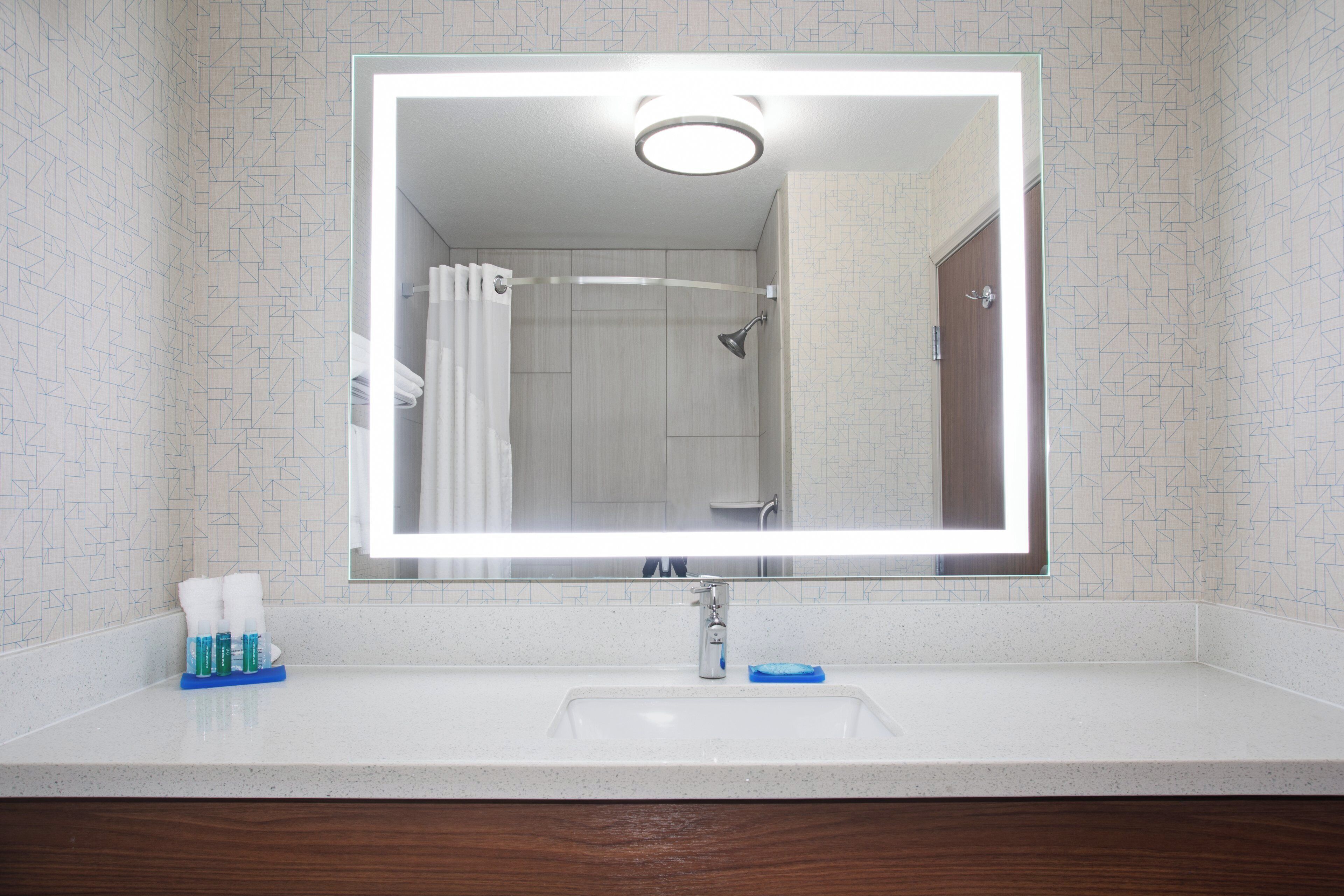 A bathroom with a large mirror, a sink, and a shower.
