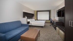 A hotel room with a blue sofa, a wooden coffee table, a bed with white linens, a desk with a computer, and a TV on the wall. - Holiday Inn Express Hotel & Suites Longmont by IHG (Longmont)