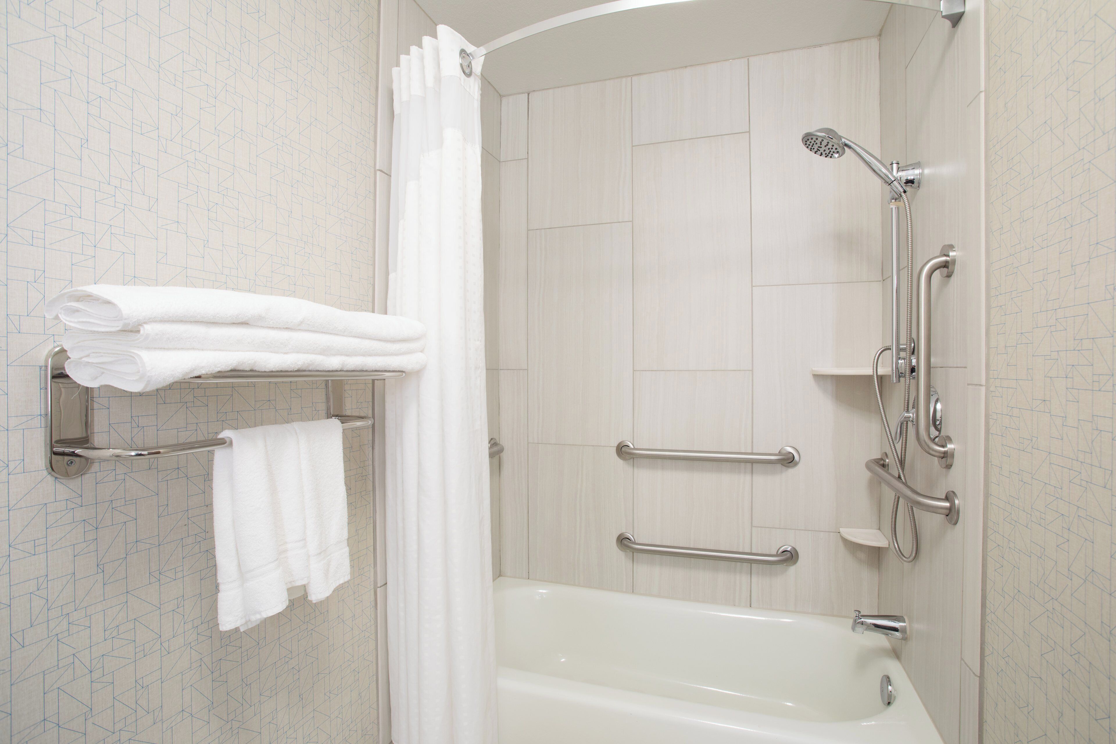 Un baño moderno con bañera, ducha y barras de apoyo.