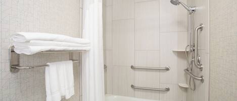 A modern bathroom with a bathtub, shower, and handrails.
