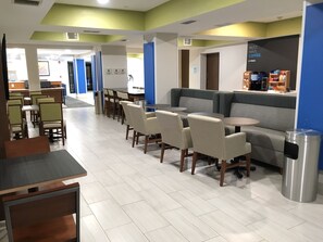Una cafeteria moderna amb zones d'aixoplugament que inclouen taules i cadires, un espai per preparar cafè i un cendrer.