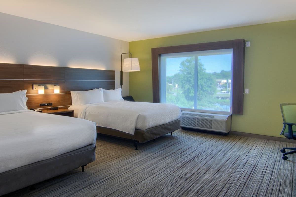 A hotel room with two beds, a nightstand, a lamp, and a large window with a view.