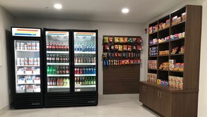 Een kamer met twee drankkoelkasten vol met diverse dranken, een muur met hangende snacks en een kast met cornflakes.