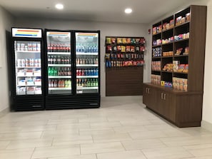A room with two beverage refrigerators stocked with various drinks, a snack wall with hanging bags, and a cabinet with cereal boxes. - Holiday Inn Express Hotel & Suites Quincy I-10 by IHG (Quincy)