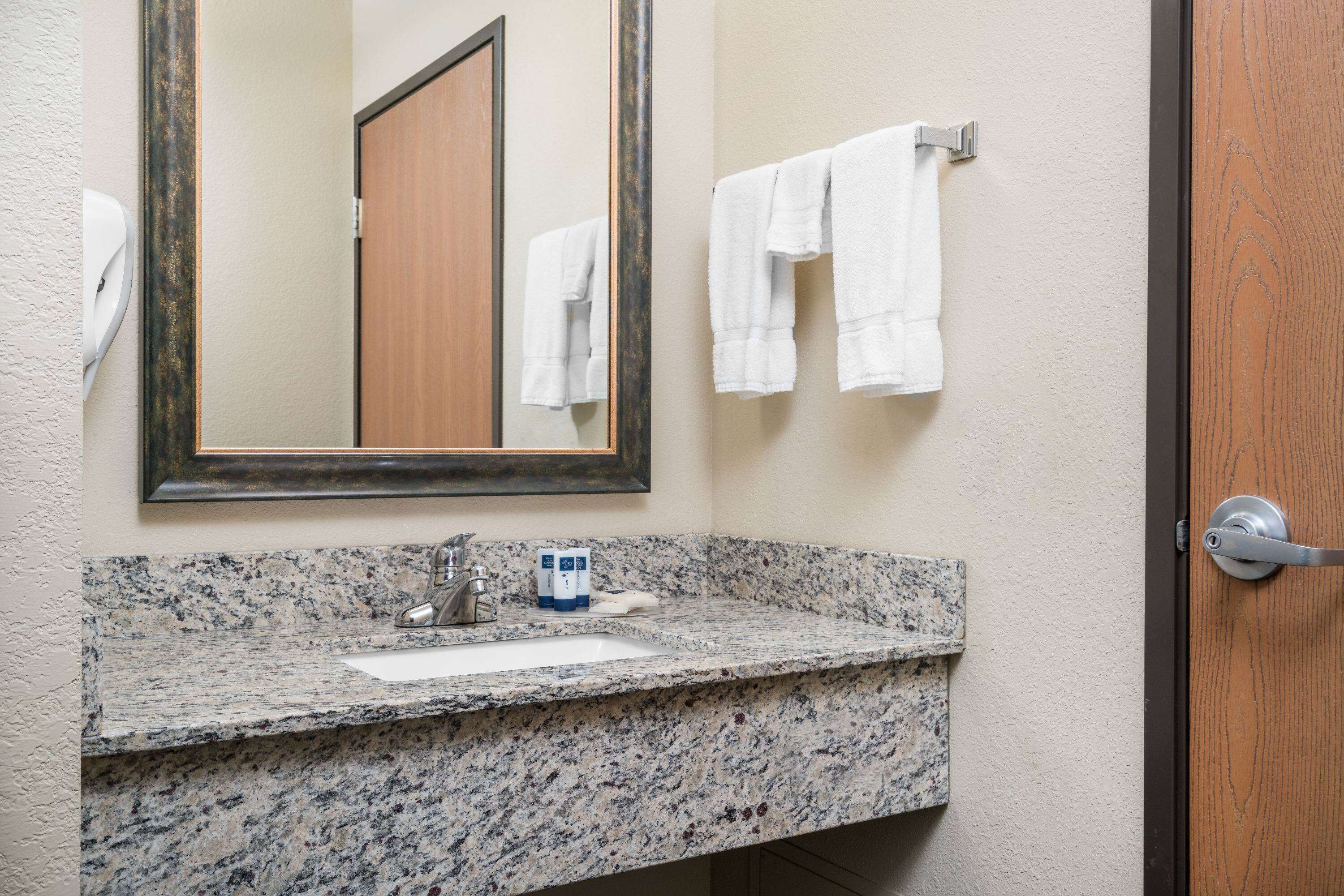 A bathroom with a granite countertop, a sink, a mirror, and two white towels hanging on hooks.
