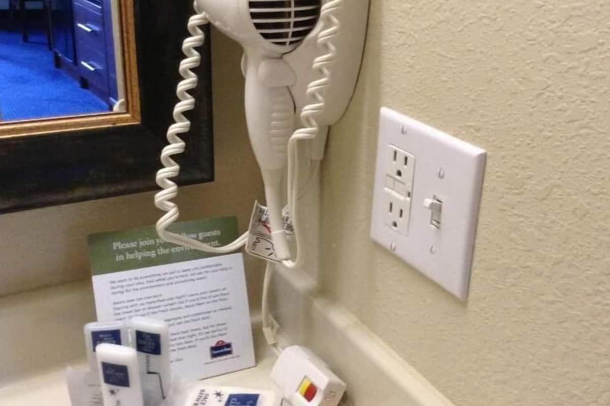 A hairdryer plugged into a wall socket, a sign requesting guests to help the environment, and a power outlet with multiple plugs.