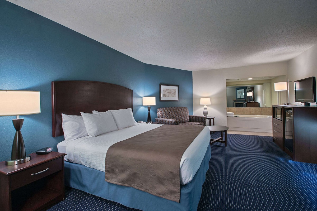 A hotel room with a large bed, bedside lamps, a chair, a desk, a mirror, and a TV.