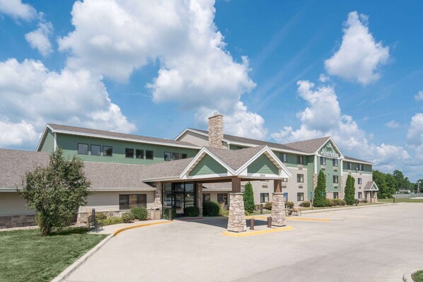 A multi-story hotel with a covered entrance, stone pillars, and a green and beige color scheme. - AmericInn by Wyndham Fort Dodge (Fort Dodge)