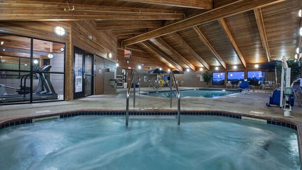 Una piscina interior con techo de madera y equipo de ejercicio al fondo.