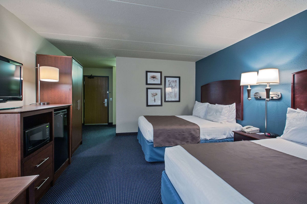 A hotel room with two beds, a desk with a television, a microwave, and a lamp.