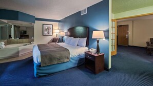 Un cuarto de hotel con una cama grande, lámparas de noche, una mesita de noche, un escritorio con lámpara, una silla, un baño con bañera y un espejo.