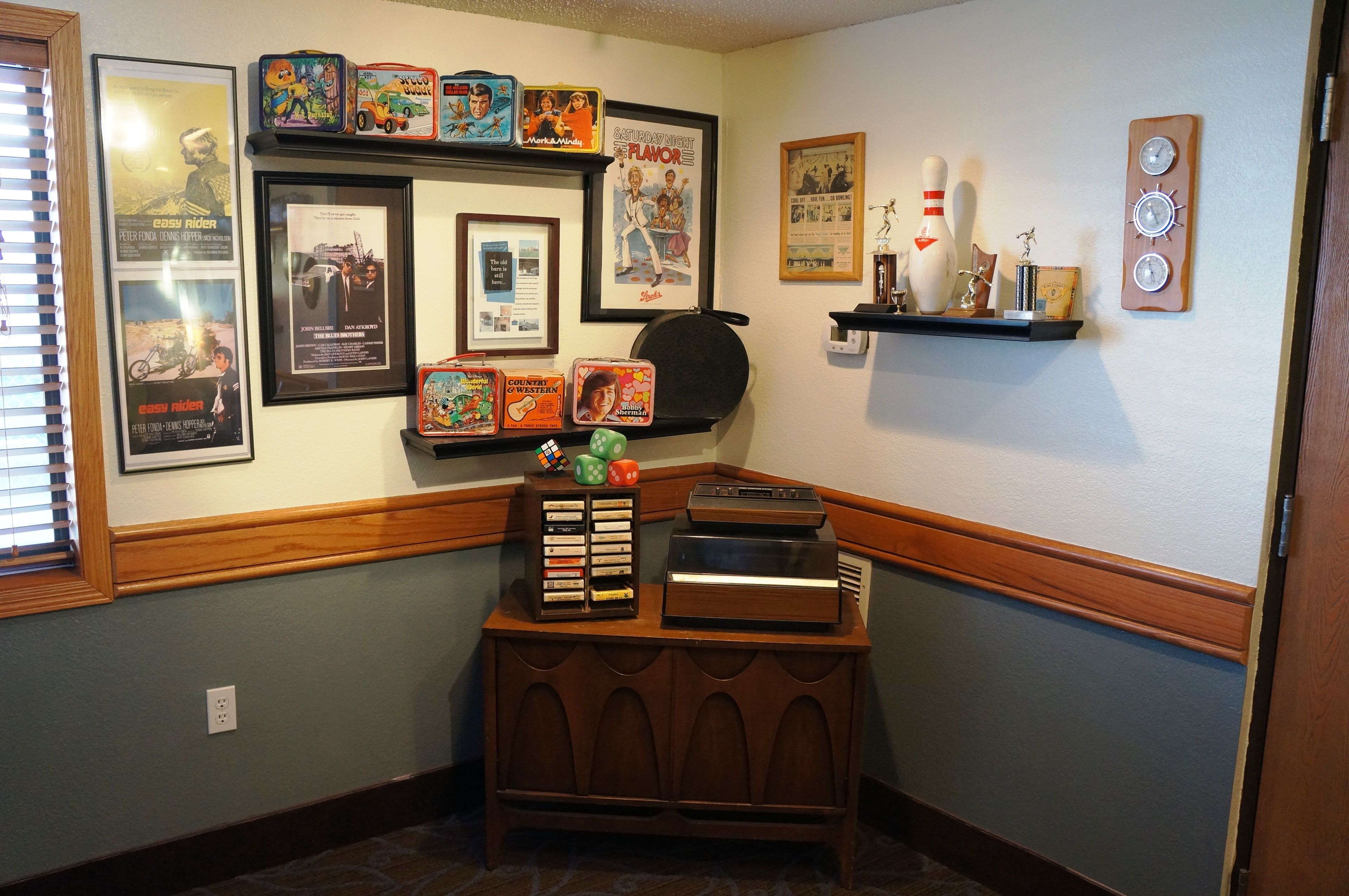A room with a wooden cabinet displaying various items, a wall with framed movie posters, and a shelf with decorative objects.