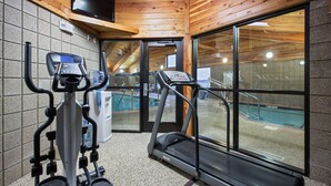 Un gimnasio con equipo de ejercicio, televisión y vista a una piscina cubierta.