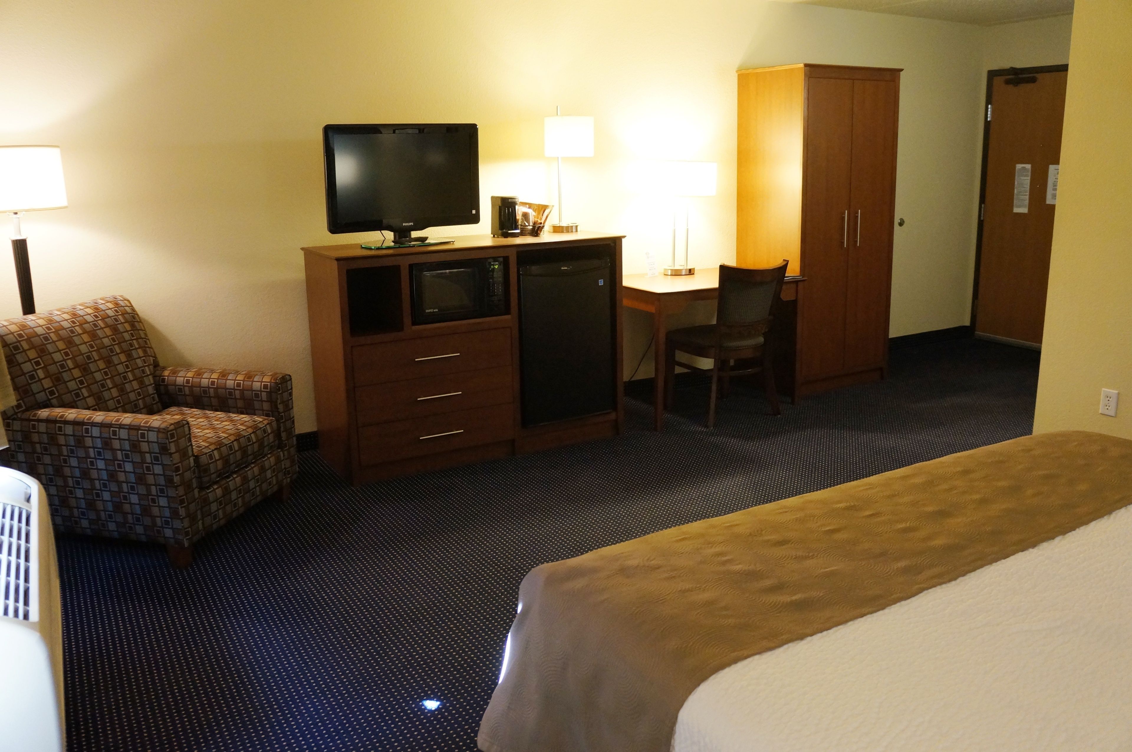 Una habitación de hotel con cama, escritorio con televisor, silla, armario y microondas.
