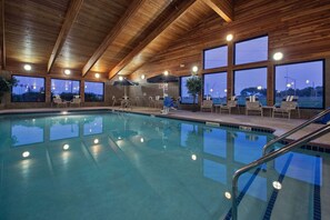 An indoor swimming pool with wooden ceiling beams, large windows, and lounge chairs. - AmericInn by Wyndham Fort Dodge (Fort Dodge)