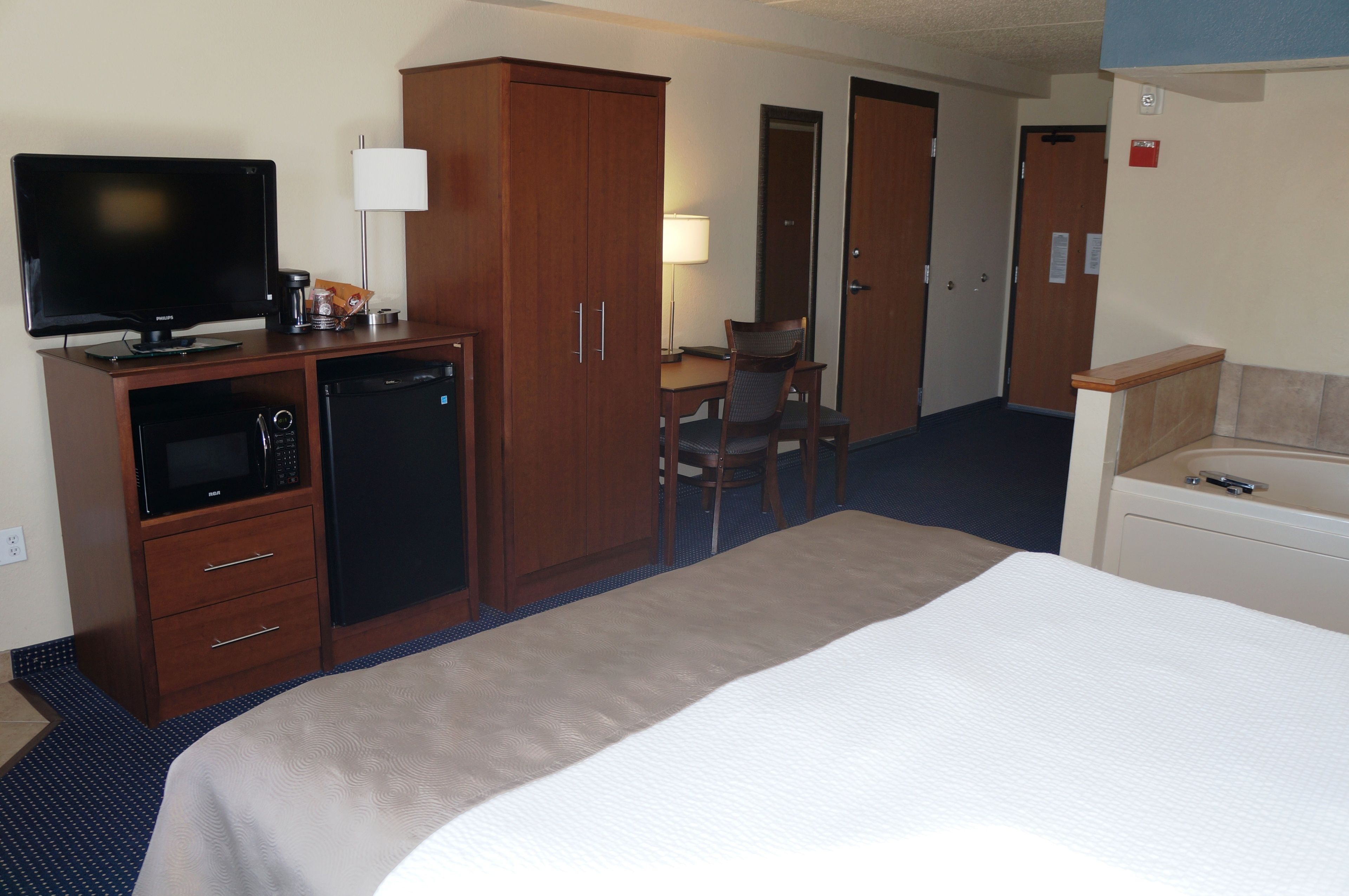 A hotel room with a bed, a desk with a computer, a television, a refrigerator, and a wardrobe.