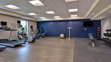 A gym with treadmills, elliptical machines, a stationary bike, a rowing machine, a bench press, a medicine ball, and a rack of dumbbells.