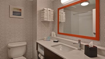 Une salle de bain avec des toilettes, un lavabo et un miroir. On y trouve des serviettes et des articles de toilette sur le comptoir.